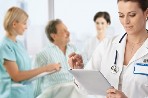 a woman in a doctor's coat is looking at a tablet.