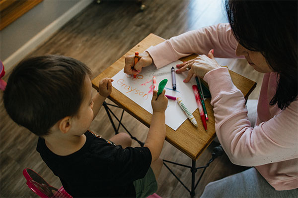 a woman and a child sitting at a table with crayons.