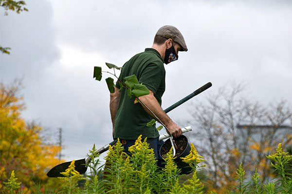 a man in a green shirt holding a pair of gardening tools.