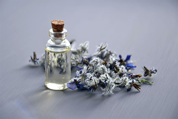 a bottle of essential oils with dried flowers on a table.