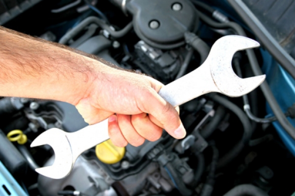 a man holding a wrench in front of a car engine.